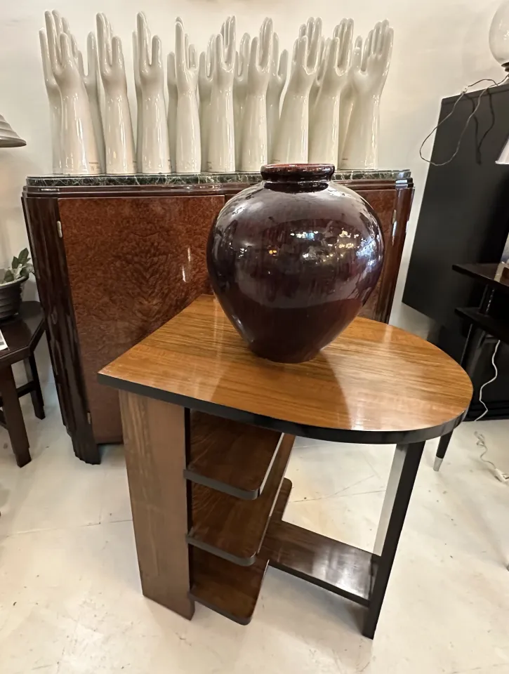 Vase en céramique ancienne de couleur foncée sur une table moderne, arrière-plan avec des mains en céramique blanche.