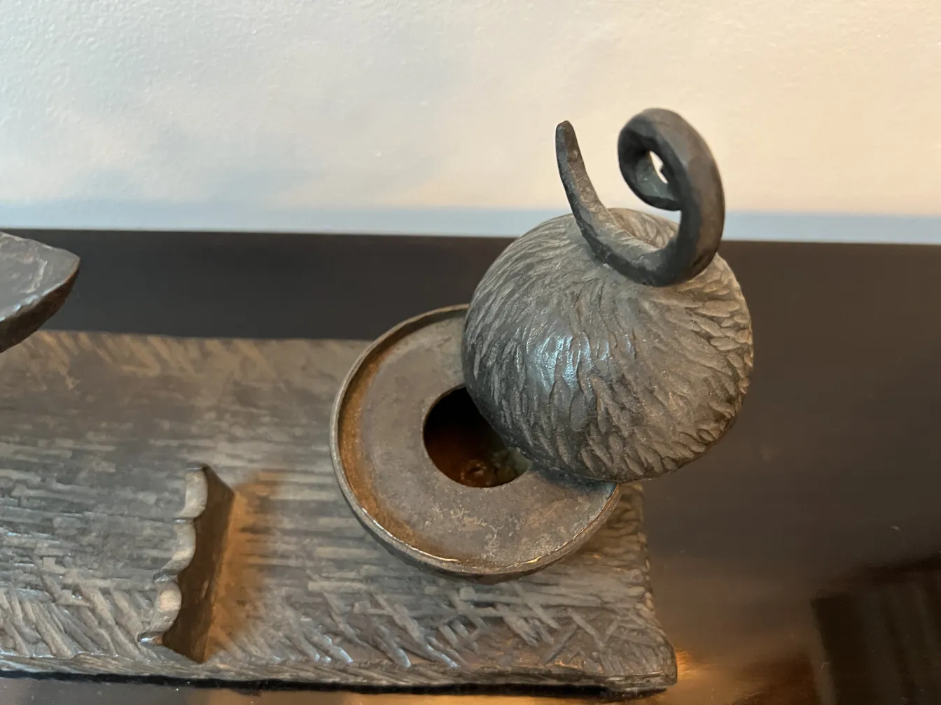 Escultura antiga com formato redondo e detalhes curvados sobre base decorativa.