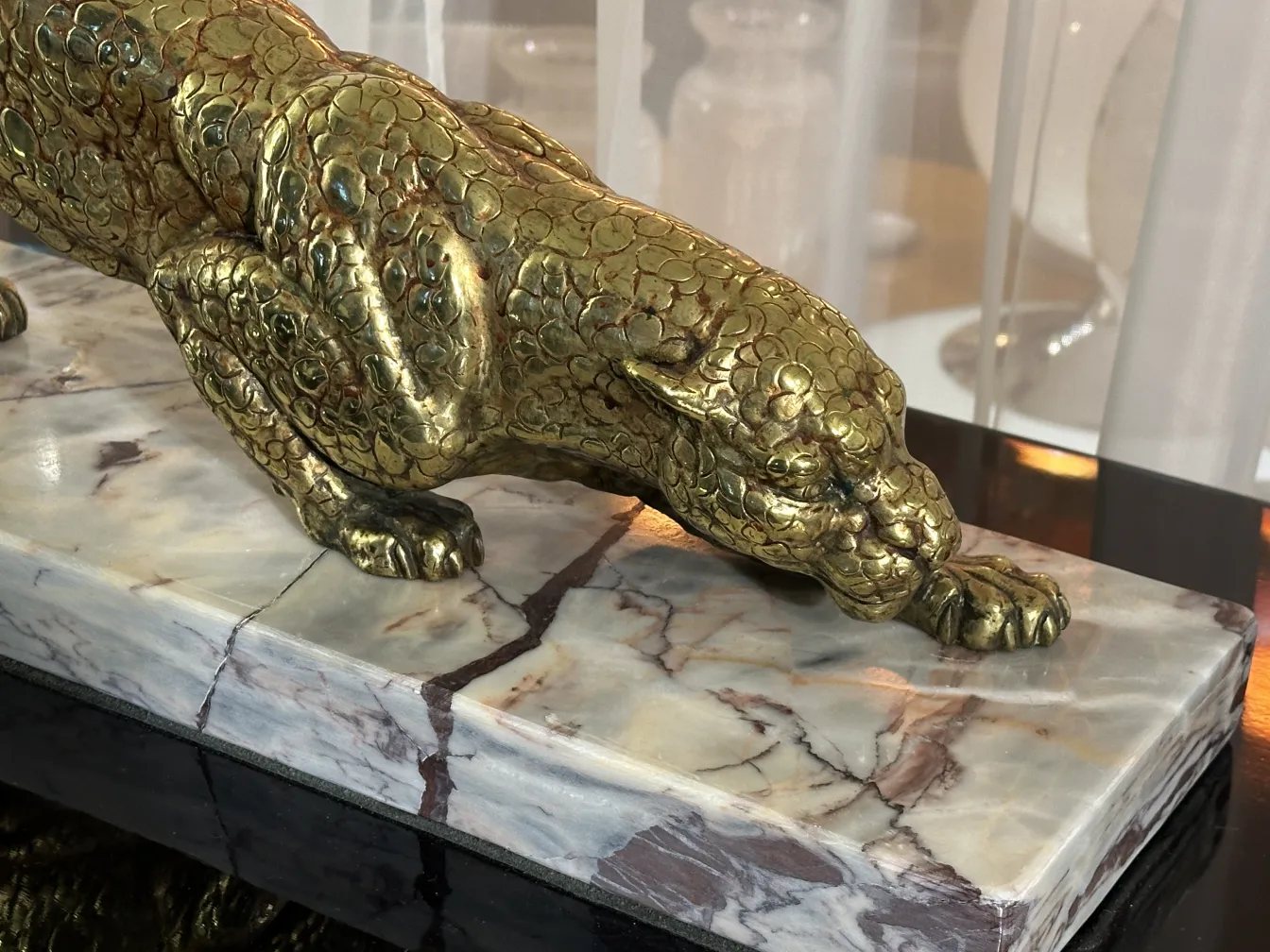 escultura antigua de felino dorado sobre base de mármol