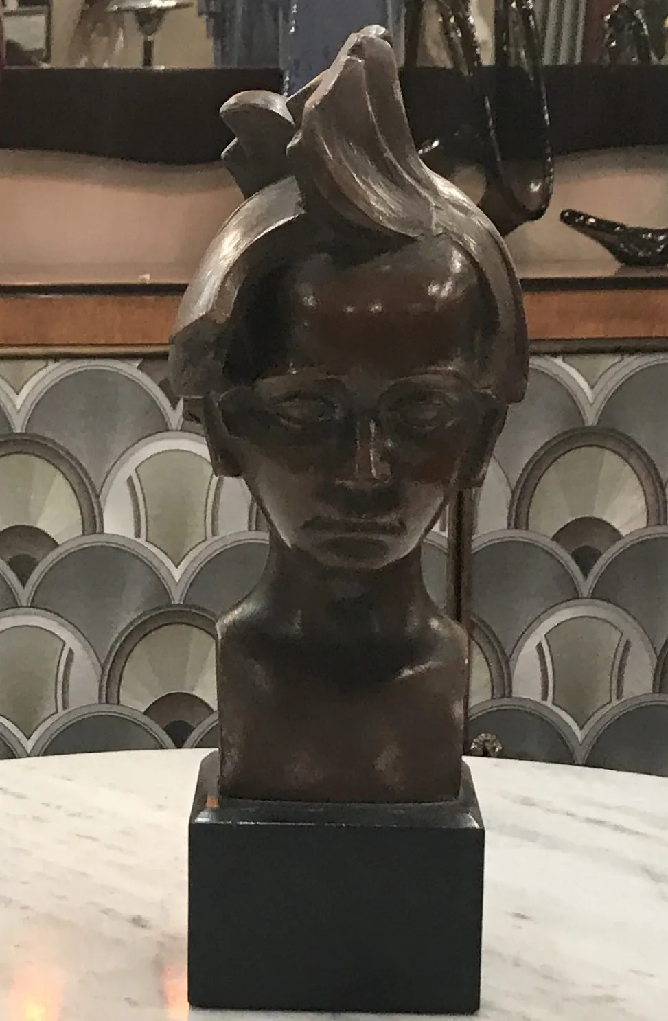 escultura antiga de figura humana com expressão séria, fundo decorado