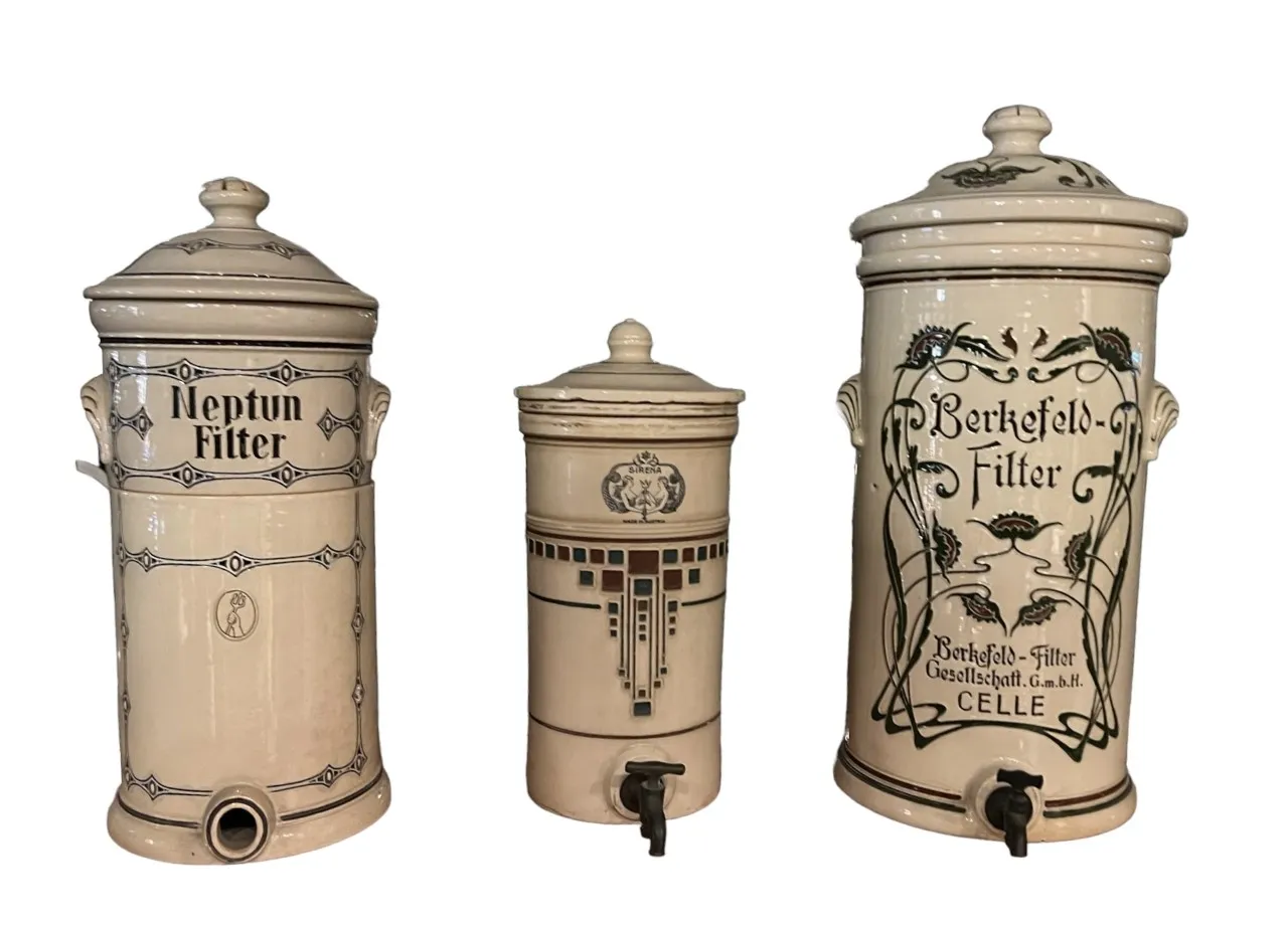 Trois pièces anciennes en céramique de filtration avec couvercles et robinets, ornées de lettres et de motifs dans différents styles.