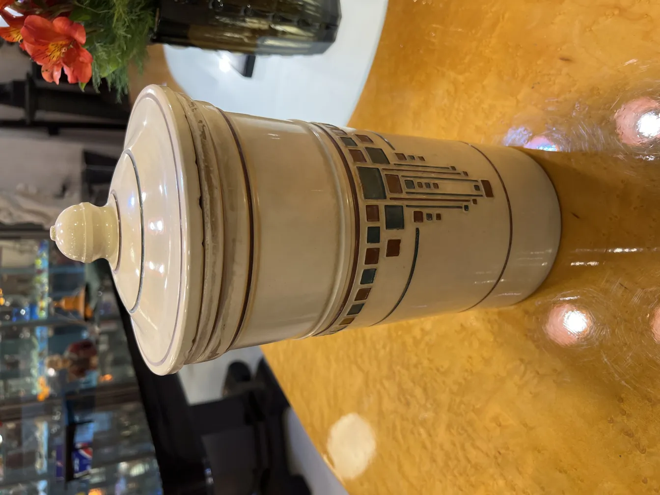 Antike Keramik mit dekorativem Deckel und detaillierten Mustern, umgeben von Blumen.