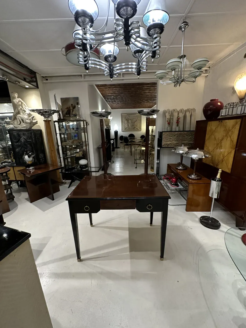 Escritorio antiguo con superficie oscura y tiradores dorados, rodeado de otros objetos decorativos.