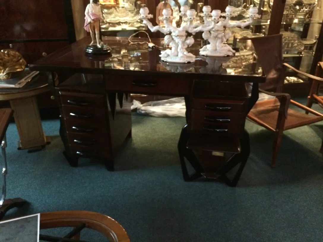 Escritorio antiguo con acabados oscuros y dibujos decorativos. Rodeado de objetos antiguos.