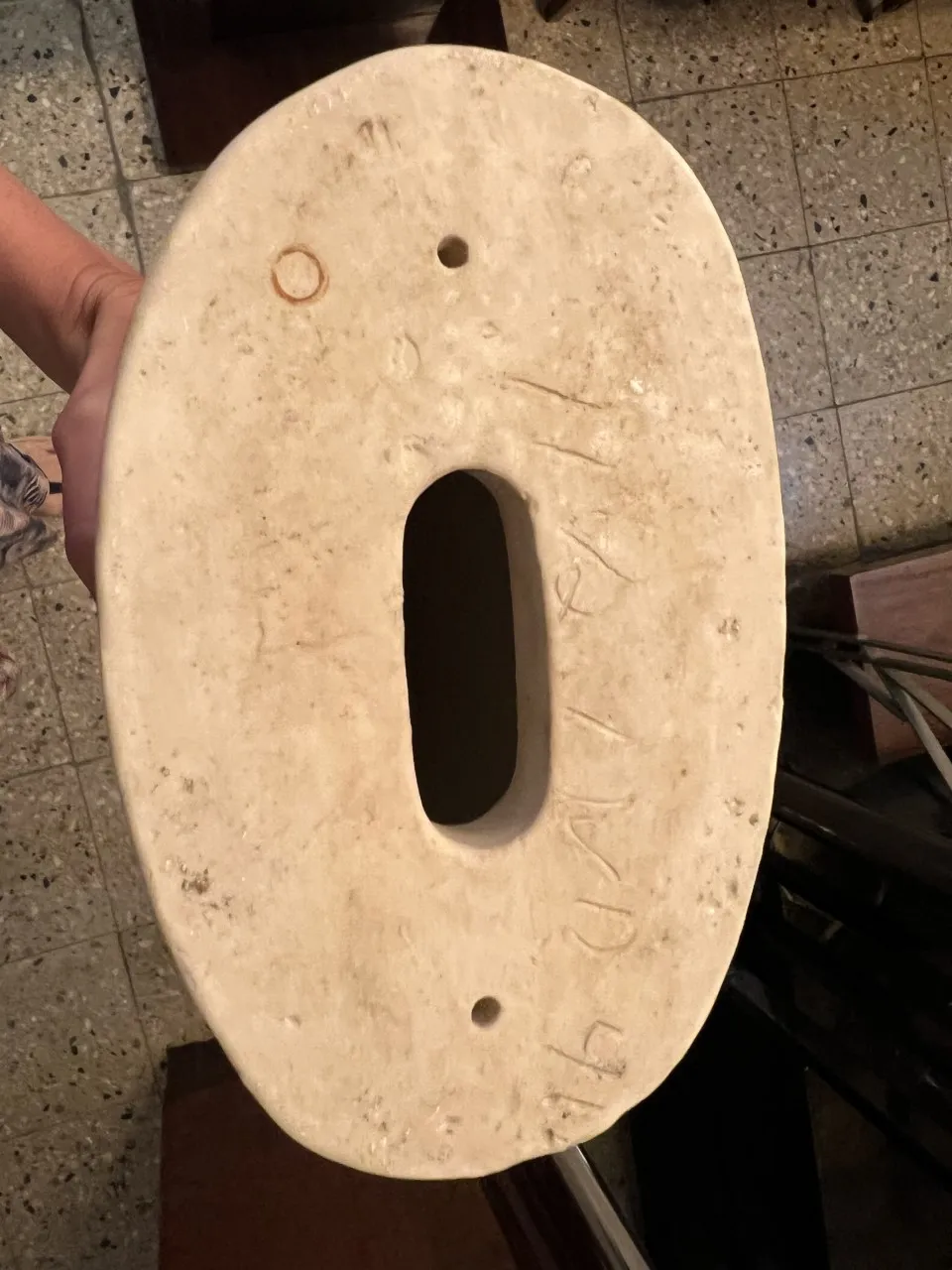 Base de cerâmica antiga com forma oval e furos, feita à mão.