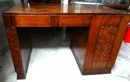 Escritorio antigo de madeira com detalhes decorativos nas laterais e acabamento polido.