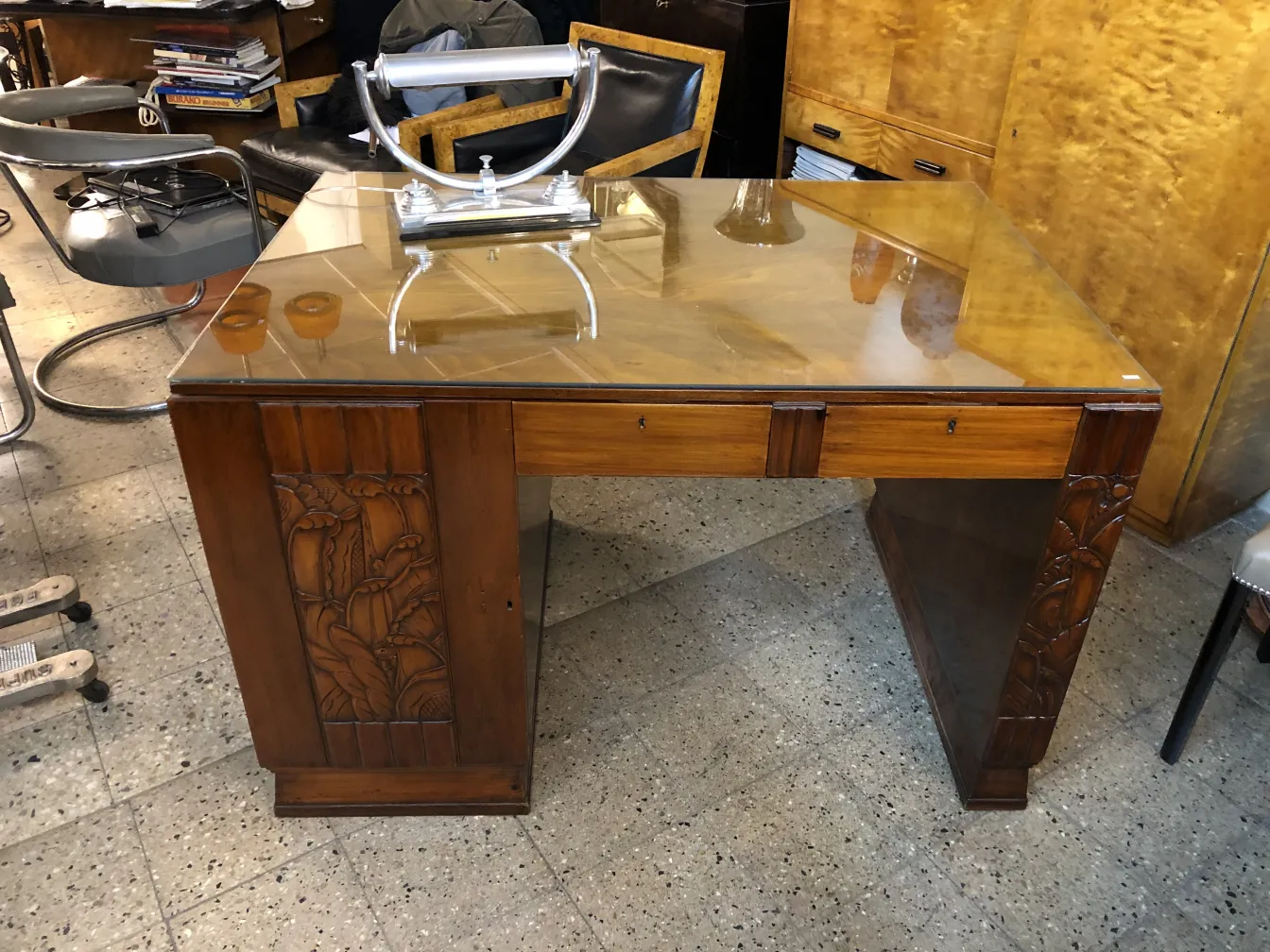 Antique wooden desk with carved details and glass top in a cozy environment.