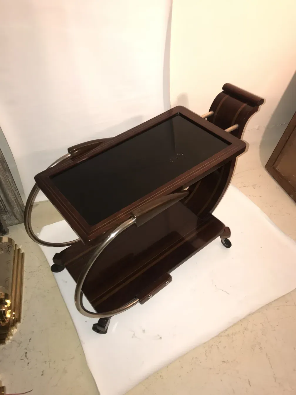 Antique cocktail trolley with glass surface and wheels, minimalist setting.
