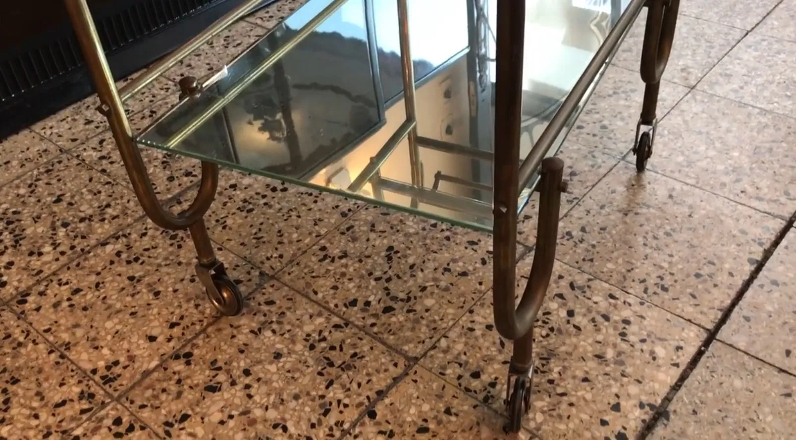 Carrello per cocktail antico con ruote e superficie in vetro, ambiente elegante.