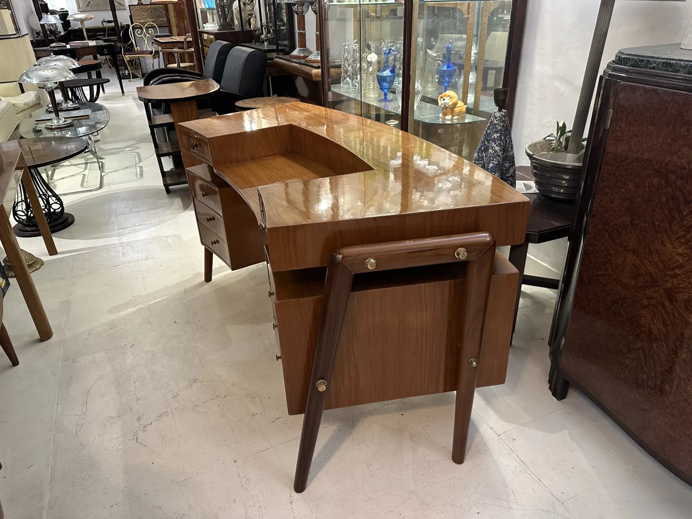 Escritorio antiguo con superficie brillante y patas de madera en tienda de antigüedades.