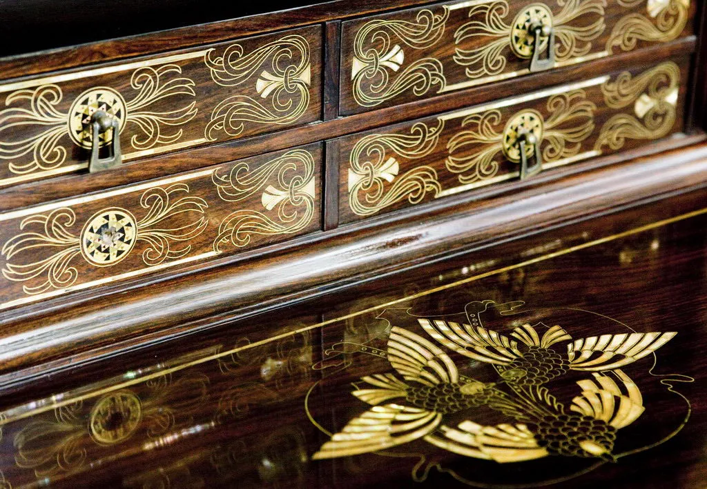 Antique desk with intricate gold designs and three drawers. Elegant design details visible.