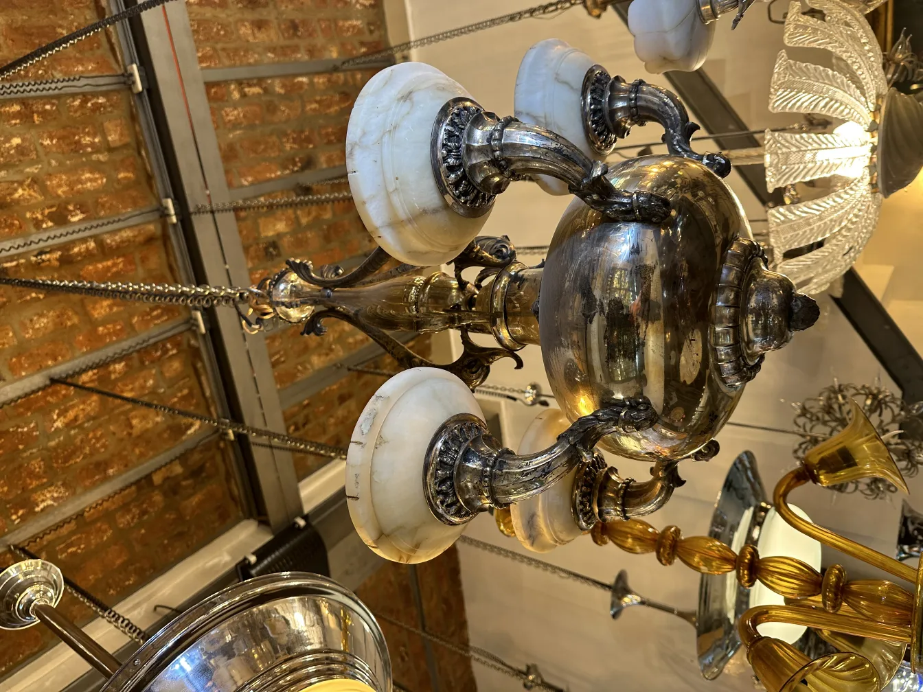 Lampada a sospensione antica con bracci decorati e tonalità chiare.