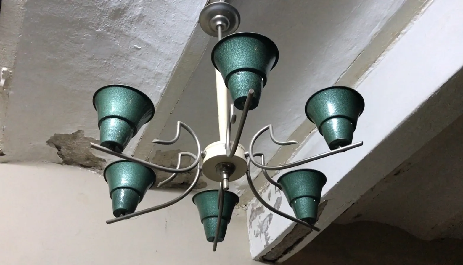 Antique hanging lamp with green finish, viewed closely in a setting with worn walls.