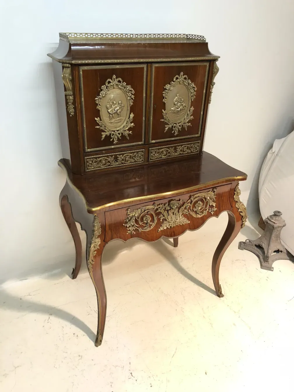 Bureau ancien avec des embellissements dorés et des jambes élégantes dans un cadre clair.