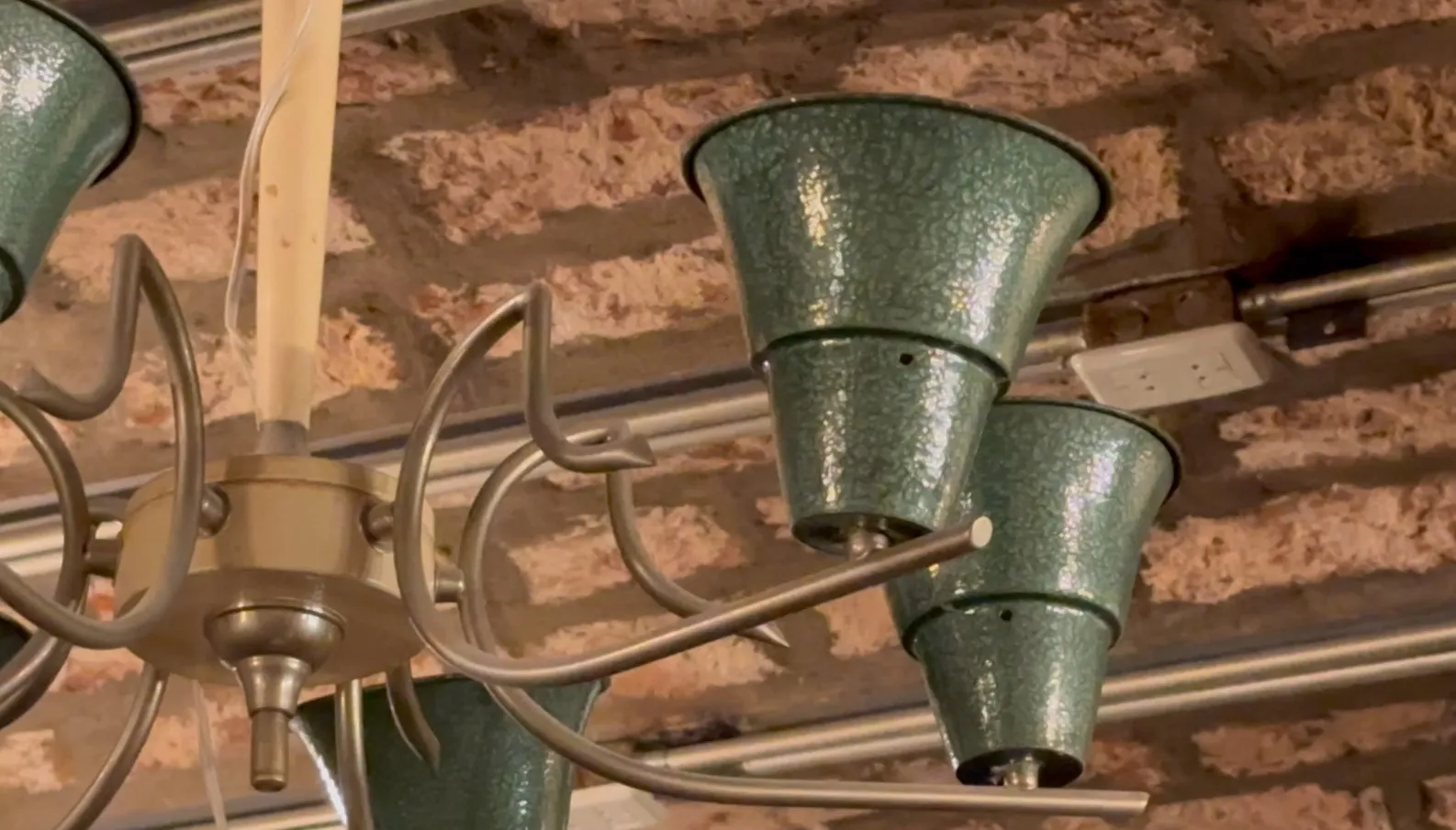 Lámpara de techo antigua de color verde brillante en un ambiente rústico con paredes de ladrillo.