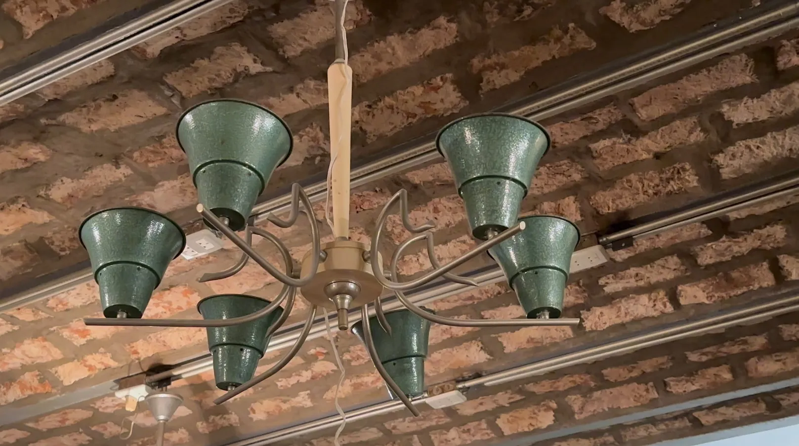 Lampada a sospensione antica con parabole verdi in un ambiente rustico.