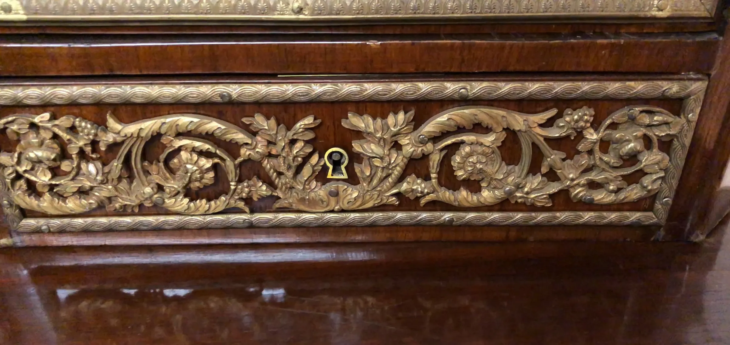 Bureau ancien en bois avec des détails en relief et une serrure dorée.