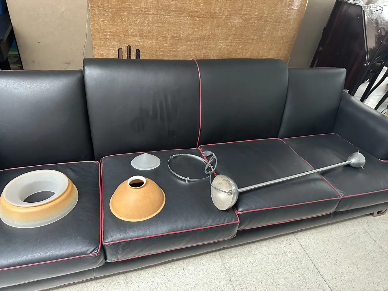 Antiga lampada de teto disposta em um sofá, com partes visíveis e um fundo bagunçado.