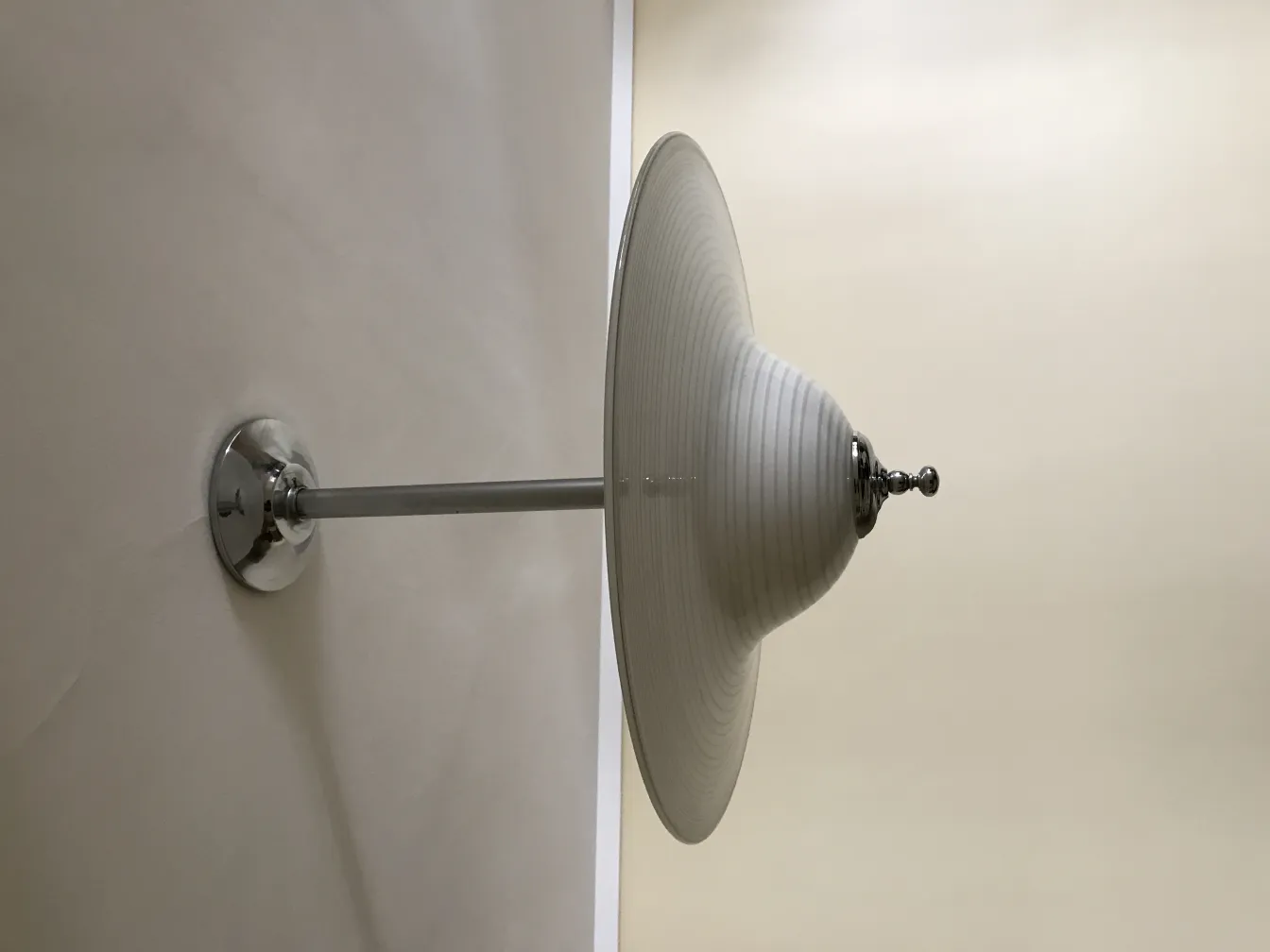 Lampada a sospensione antica con base lucida in un ambiente neutro.