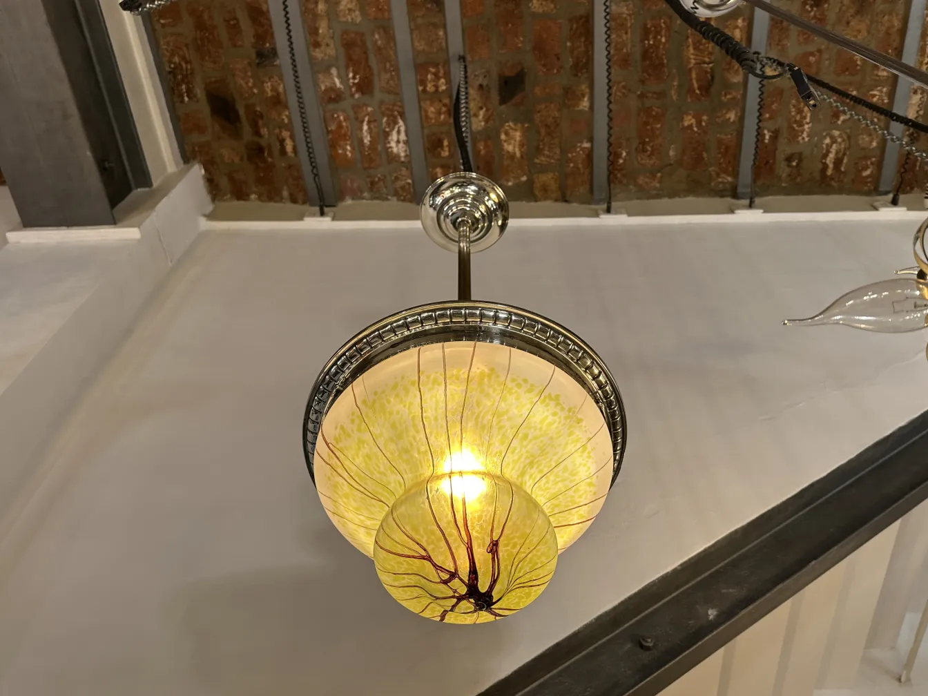 Античная подвесная лампа цвета янтаря с элегантными деталями, освещающая пространство. Видимый кирпичный фон.