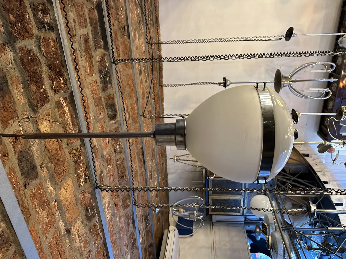 Lampada a sospensione antica in un ambiente contemporaneo, con base in metallo e paralume bianco.