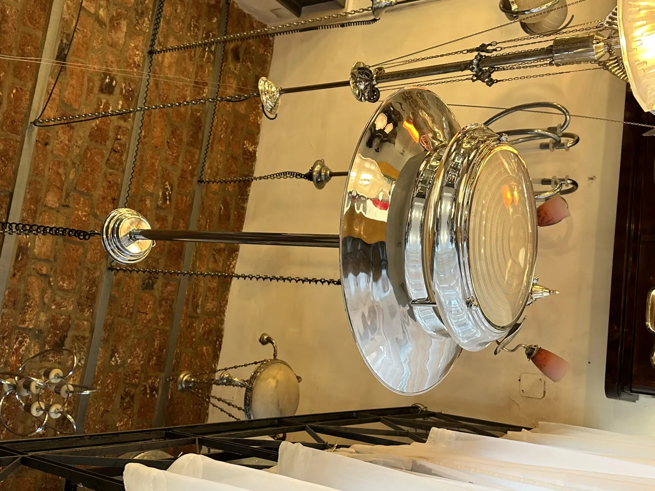 Antique hanging lamp with a glossy design, surrounded by chains and an exposed brick background.