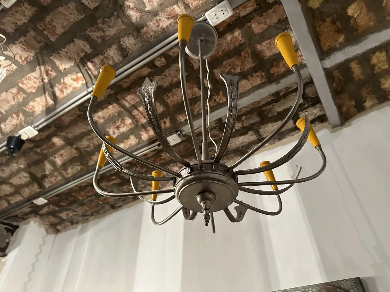 Lámpara de techo antigua con diseño elegante y brazos curvados sobre fondo de techo de ladrillo.