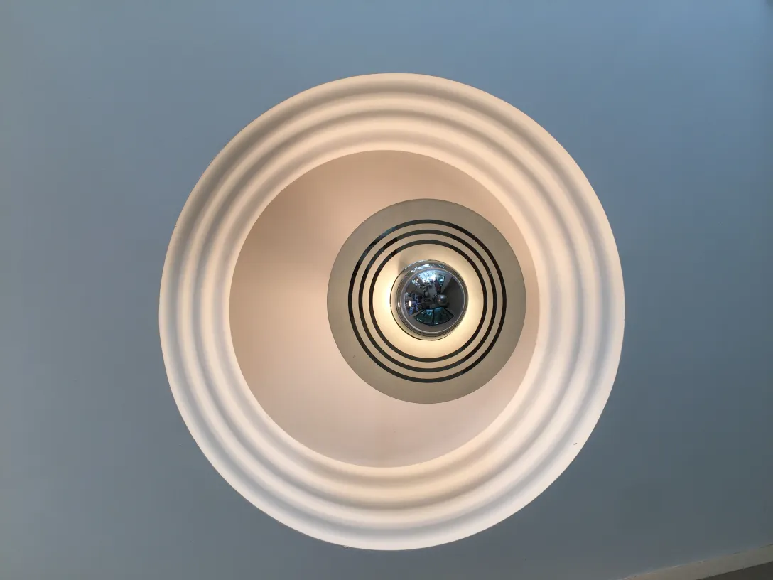 Lampada a sospensione antica con design moderno, forma circolare e dettagli al centro, che illumina uno spazio.