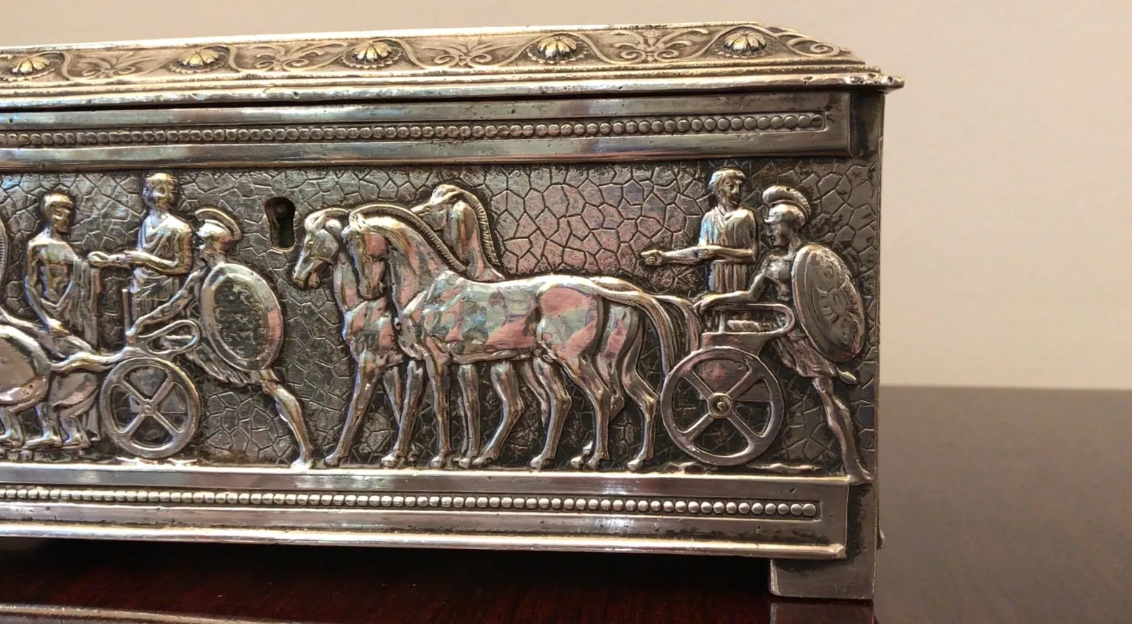 Caja antigua decorada con guerreros y caballos en relieve, perfecta para exhibición.
