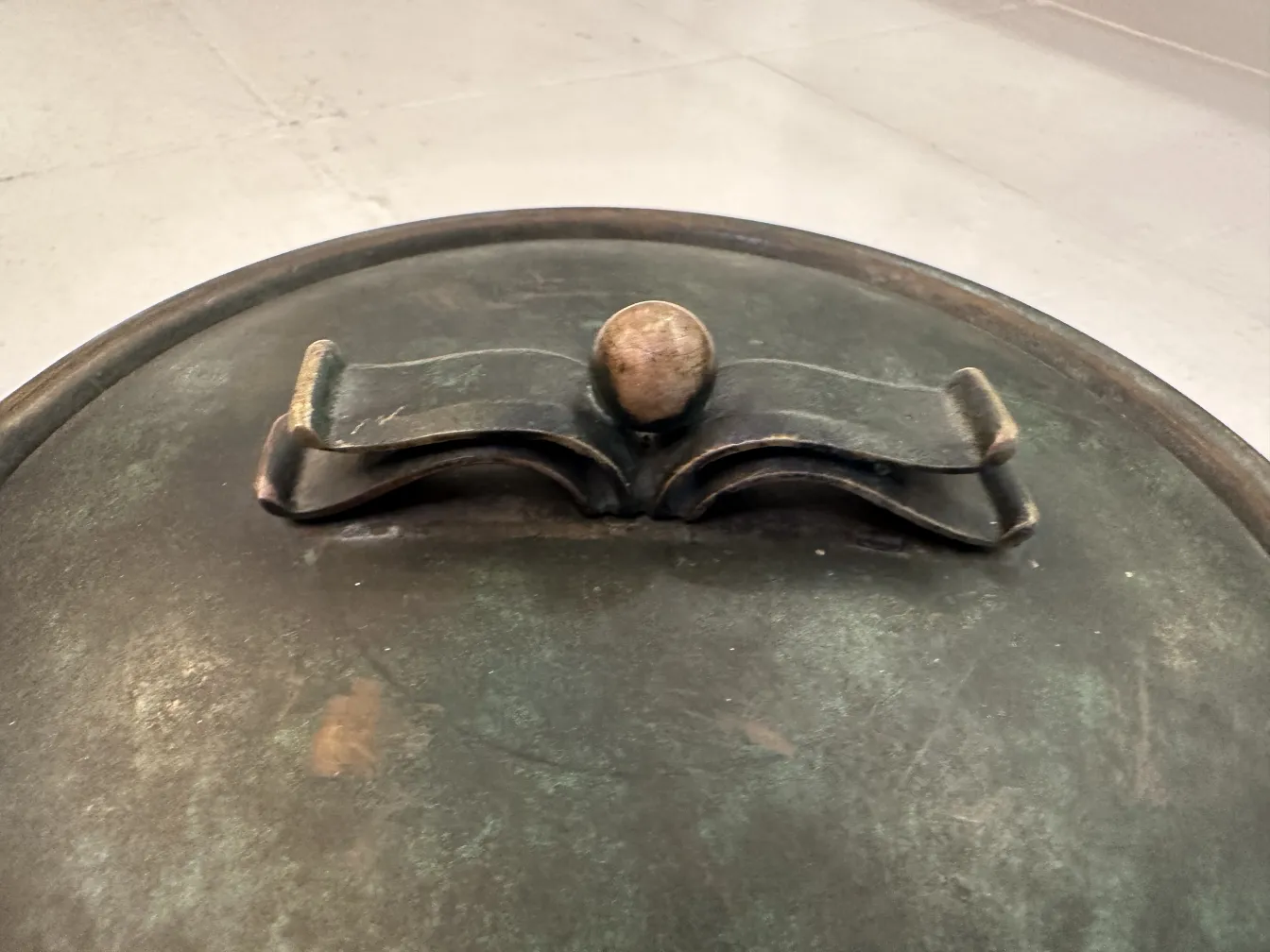 Caja antigua de metal con un diseño distintivo, tiene una tapa redonda con un asa en la parte superior.