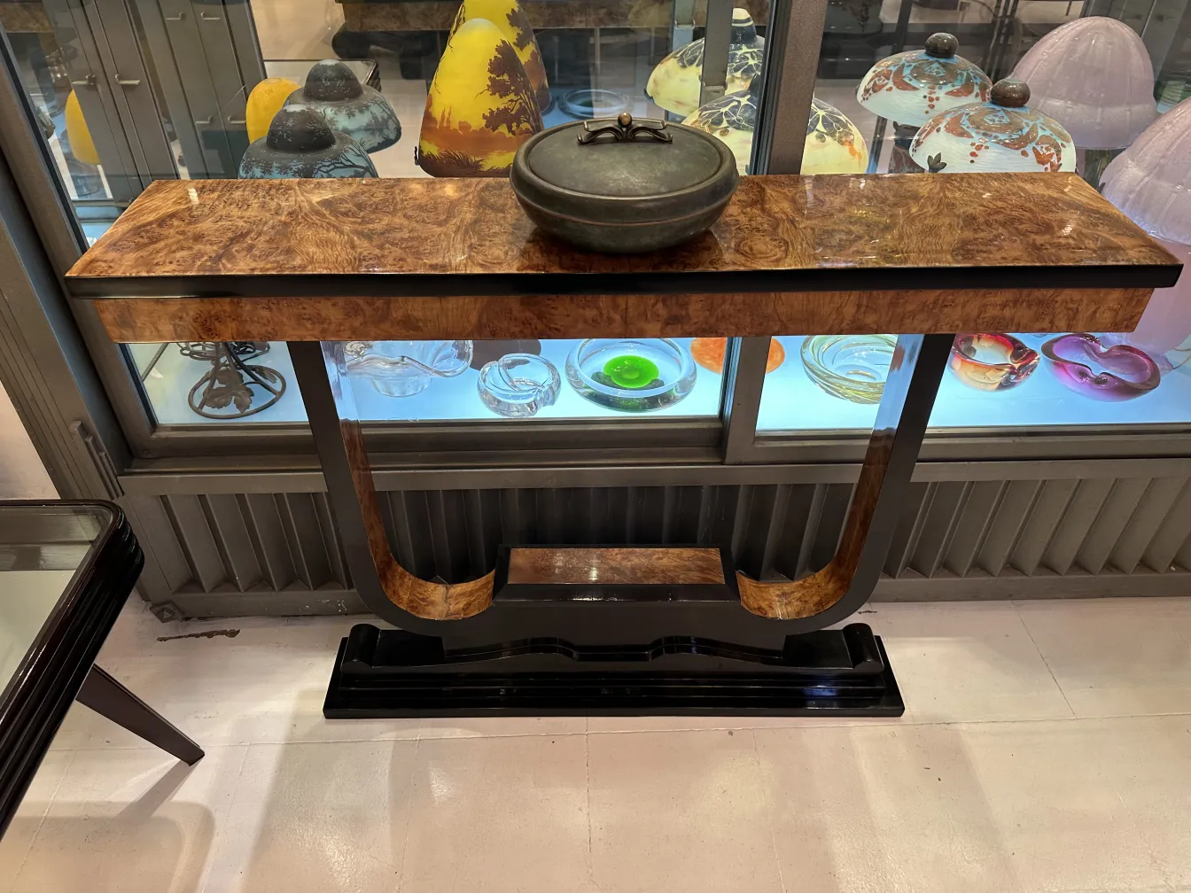 Caja antigua decorativa con tapa, situada sobre una mesa, rodeada de cristalería colorida.