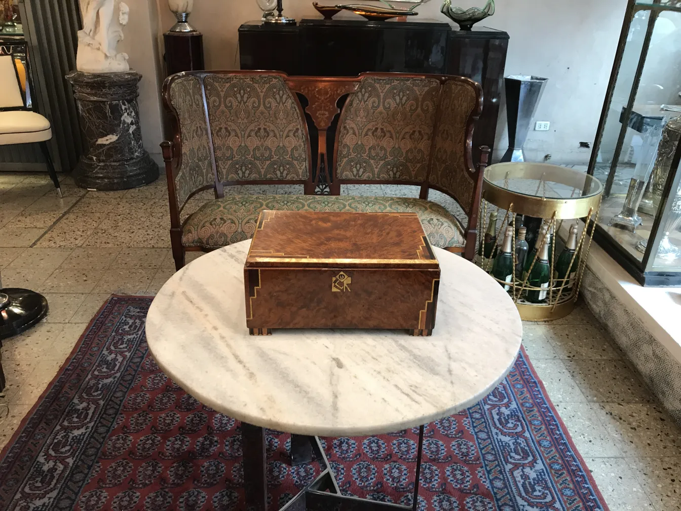 Caja antigua de madera con decoración en la tapa, sobre mesa de mármol.