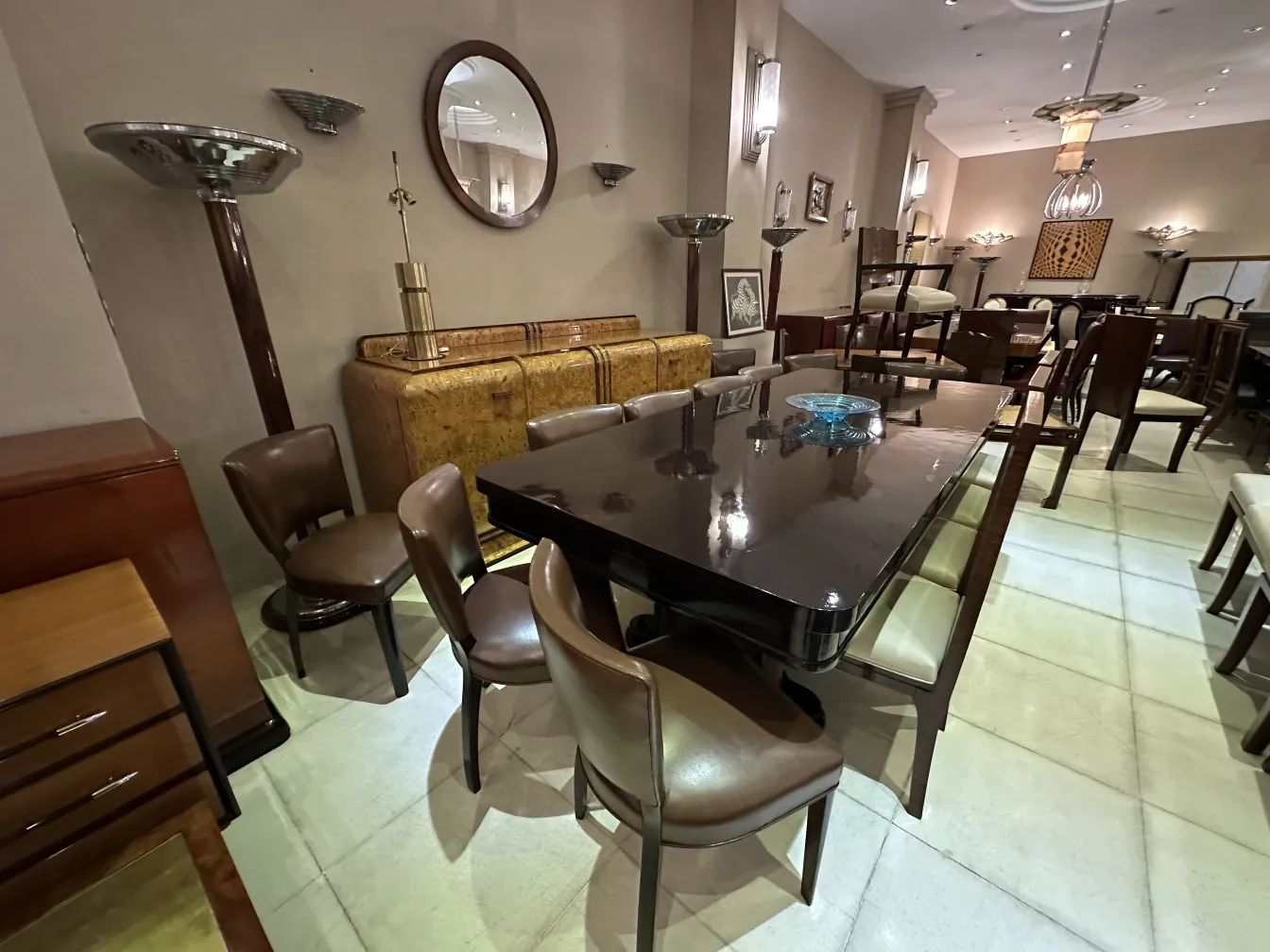 Aparador antigo com detalhes decorativos, cercado por cadeiras e mesas elegantes.