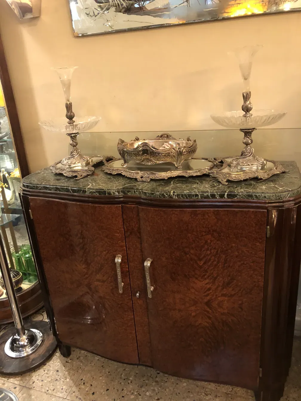 Aparador antiguo con superficie de mármol y adornos plateados, decorado con objetos de cristal.