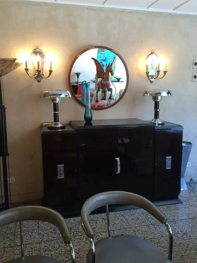 Aparador antigo com luzes brilhantes e um espelho decorativo redondo.