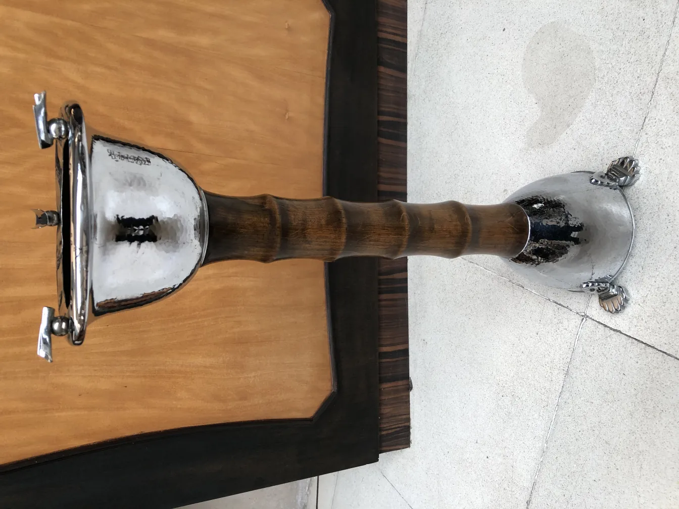 Cenicero de pie antiguo con acabado brillante y detalles decorativos en un entorno neutro.