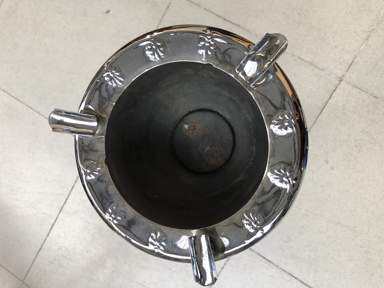 Cenicero de pie antiguo con un diseño de hojas plateadas, mostrado desde arriba en un entorno neutral.
