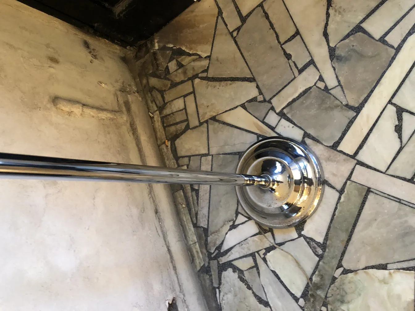 Lampada da terra antica con base metallica lucida, vicino a un pavimento a mosaico.