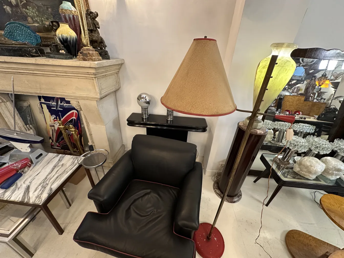 Alte Stehleuchte mit beigem Schirm in einem Raum mit schwarzem Sofa und verschiedenen Dekorationsgegenständen.