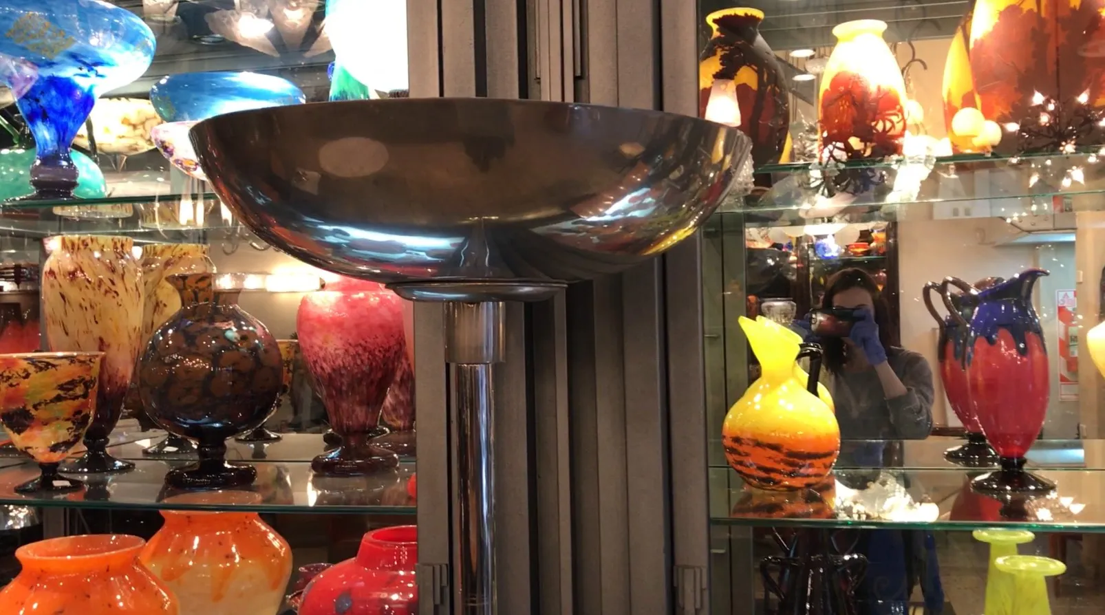 Torchiere ancienne avec un design élégant devant des vases colorés.