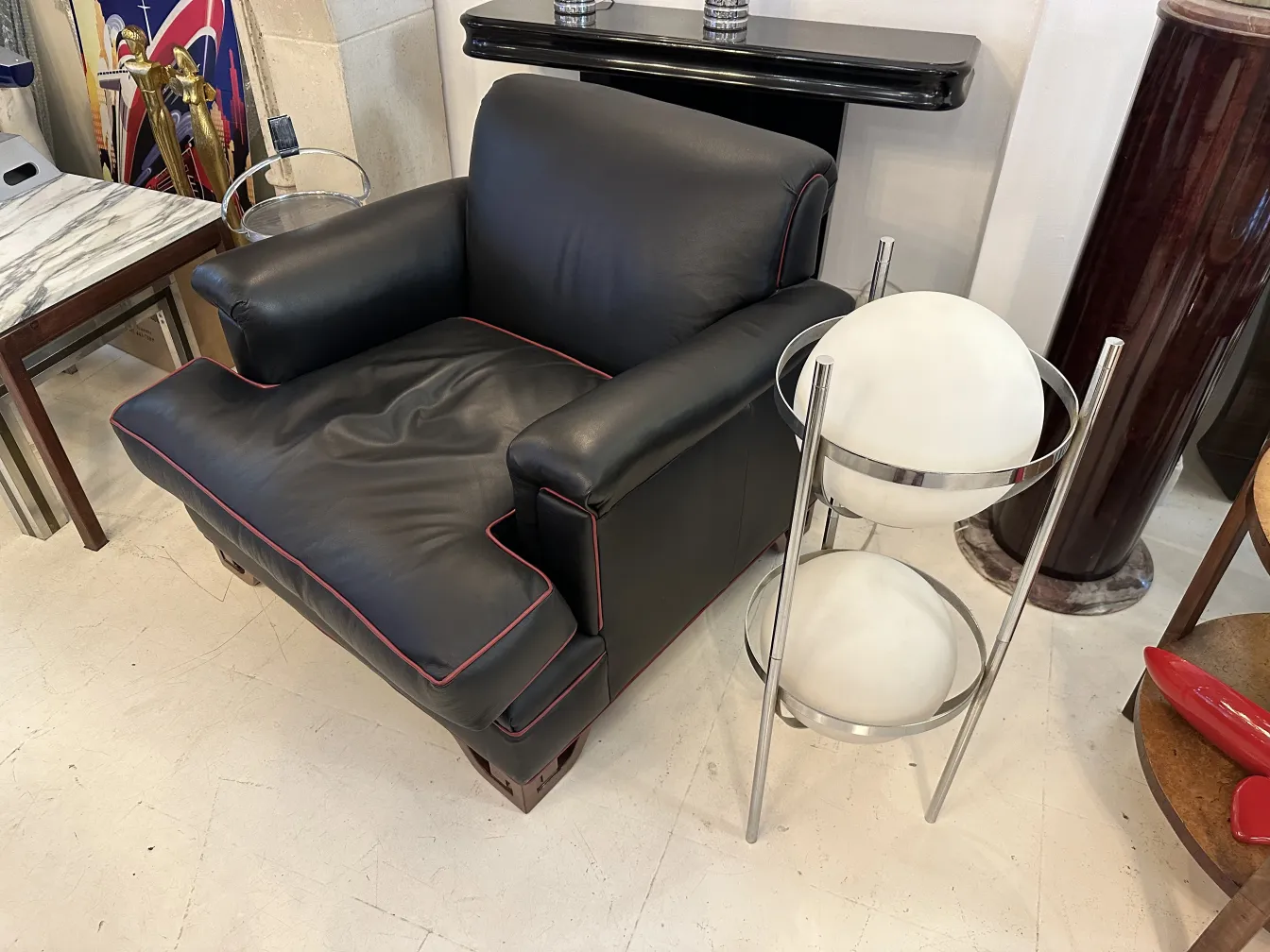 Torchiere ancienne avec sphère dans un cadre élégant près d'un fauteuil noir.