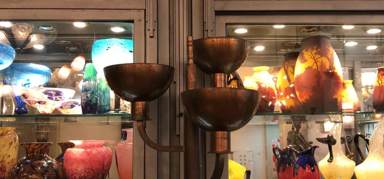 Alte Stehlampe mit zwei Öffnungen, umgeben von bunten Vasen.