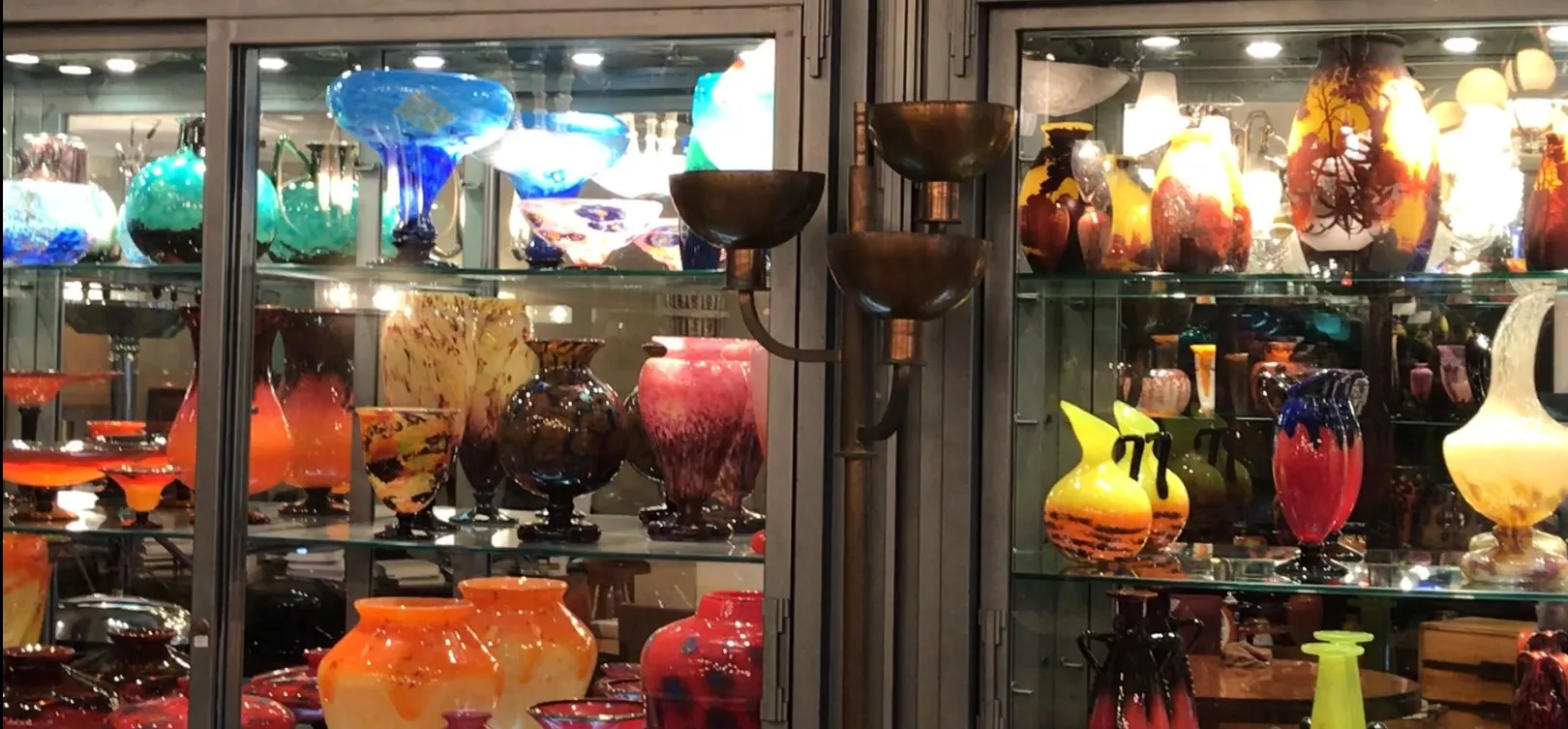 Torchiere ancienne exposée parmi des vases colorés dans une vitrine.