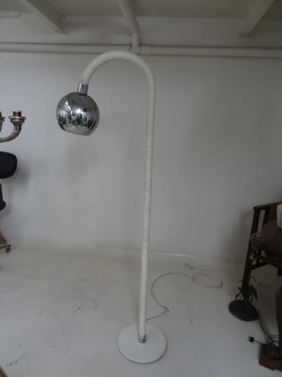 Torchiere antique avec bras courbé et base ronde dans un fond minimaliste.