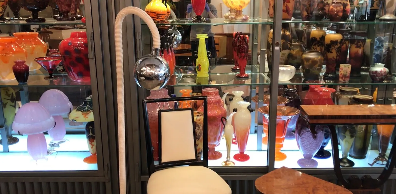 Lampada da terra antica con design elegante e sfera lucida, circondata da colorati vasi di vetro.