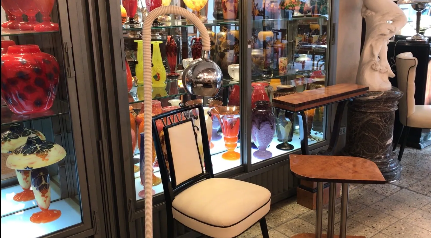 Antique floor lamp with elegant design, beside a white chair and colorful decor in the background.