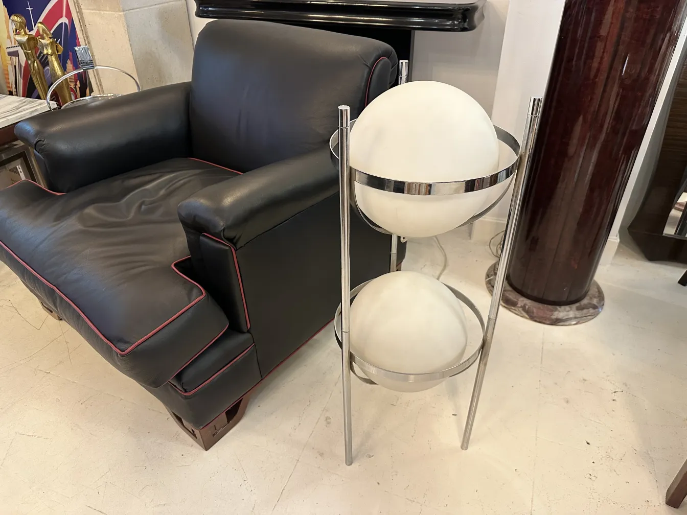 फर्श का दीपक पुराना दो सफेद गेंदों के साथ एक धातु धारक में, एक काले सोफे के साथ एक कमरे को सजाना।