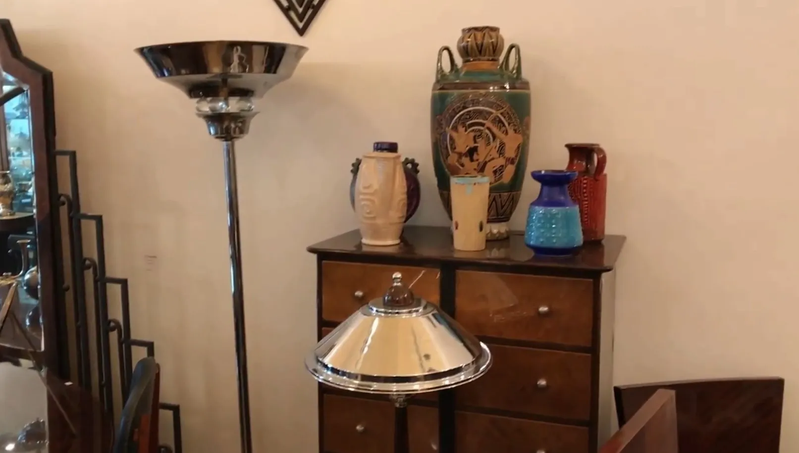 Antike Stehleuchte mit glänzendem Metallschirm, umgeben von bunten Vasen in einem eleganten Ambiente.