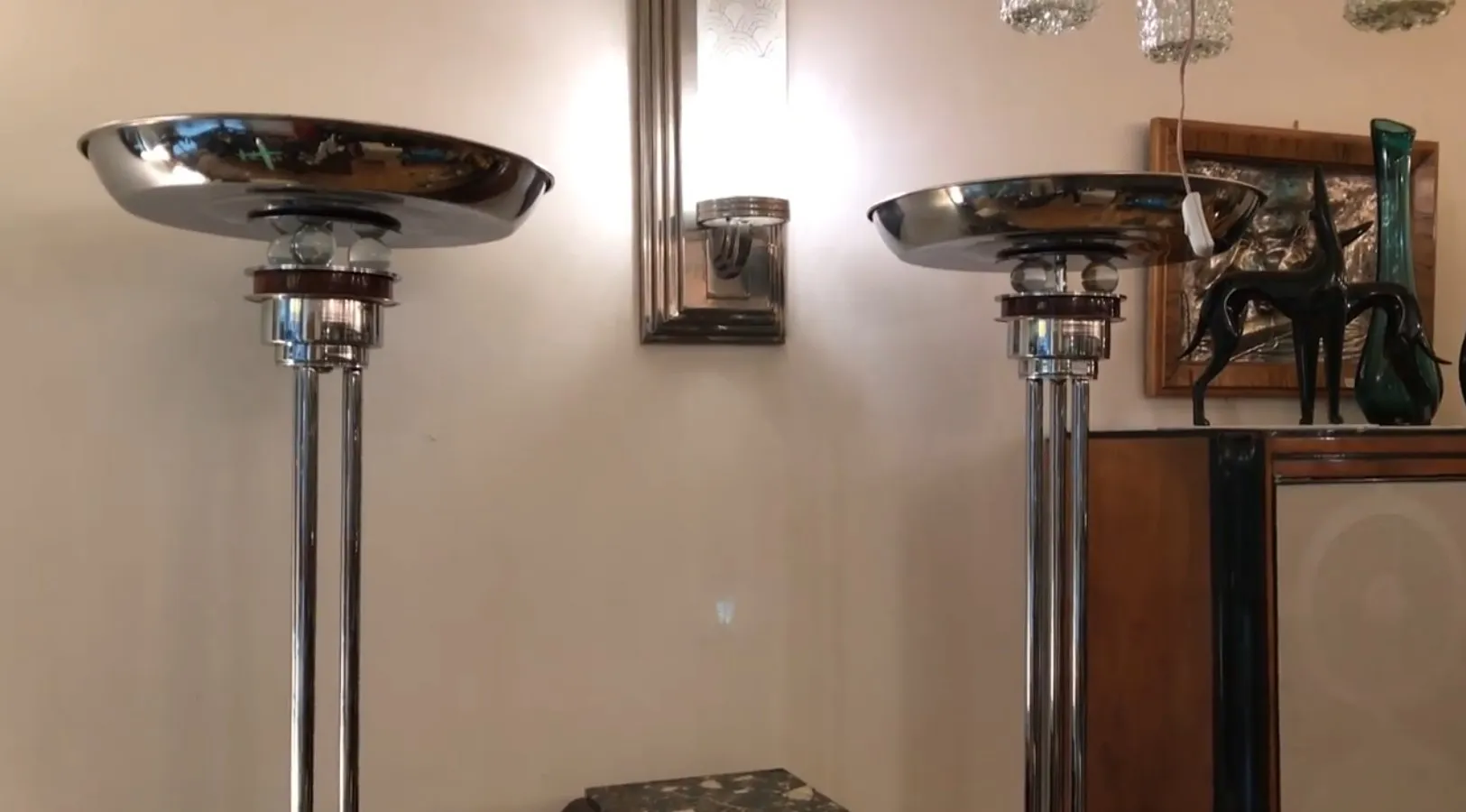 View of 2 antique floor lamps with shiny finish, in a decorative setting with wall art and other objects.