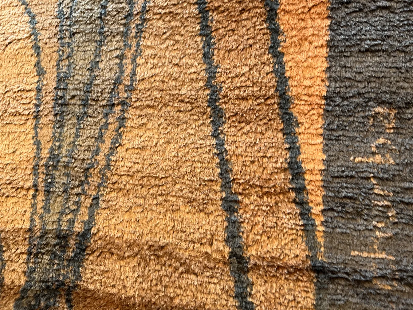 Detail eines antiken Teppichs mit warmen Farben und abstrakten Formen auf neutralem Hintergrund.